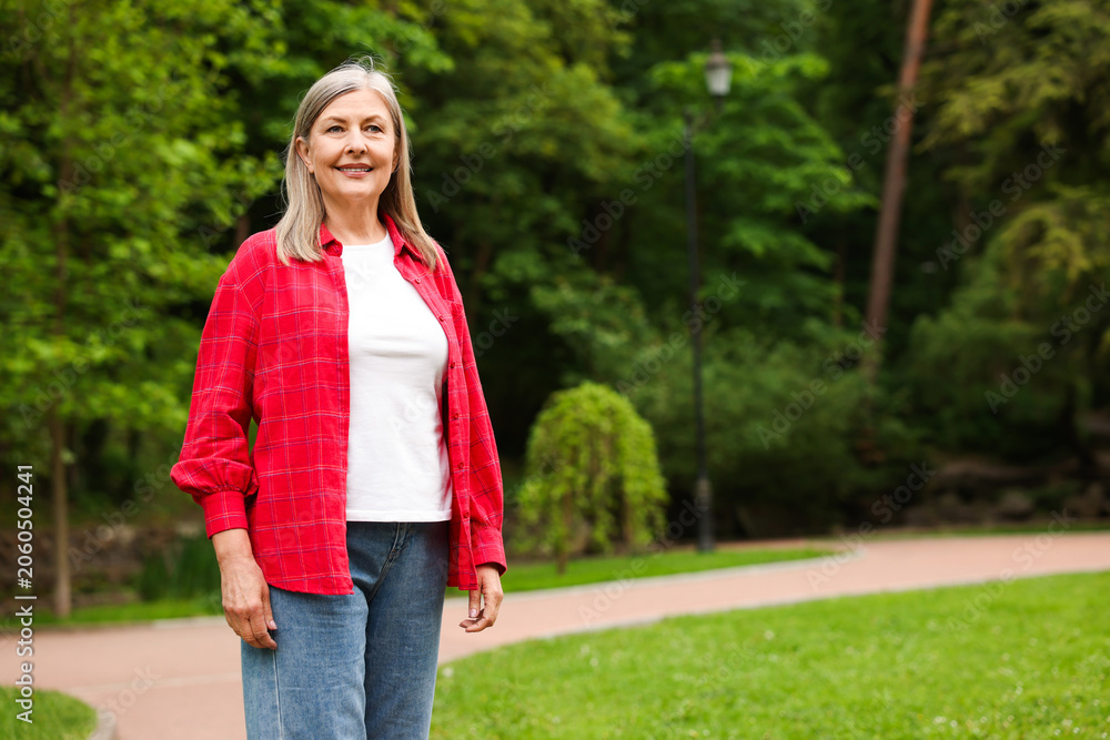 Fototapeta premium Beautiful senior woman walking in spring park, space for text