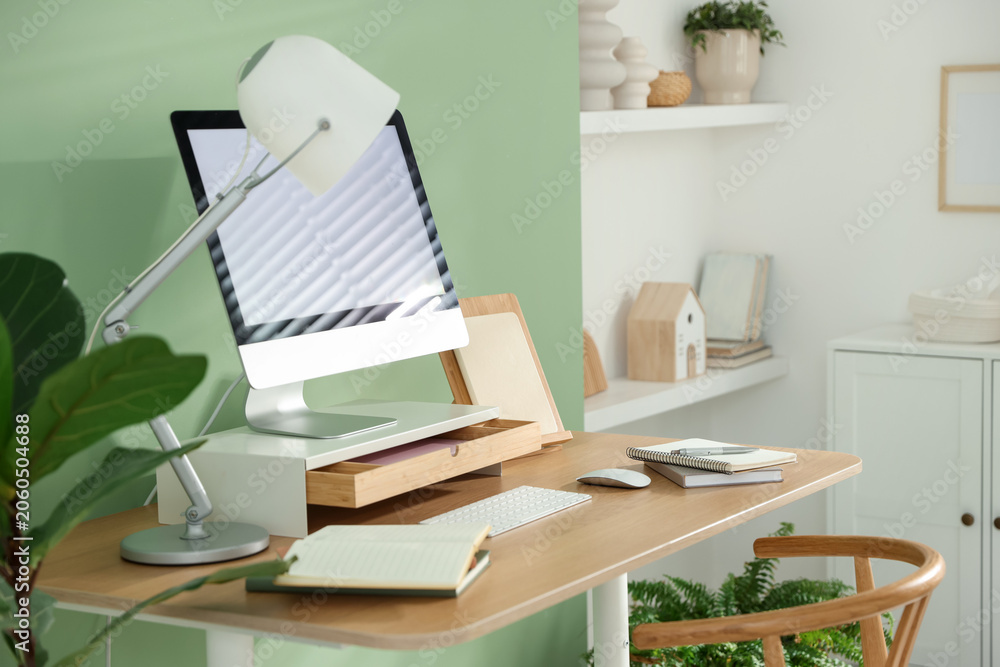 Fototapeta premium Workplace with computer monitor on riser stand, lamp and stationery indoors
