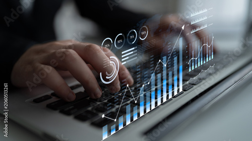 Фотография Modern Businessman Analyzing Financial Data on Laptop with Visual Analytics Overlay on Keyboard in Innovative Office Environment