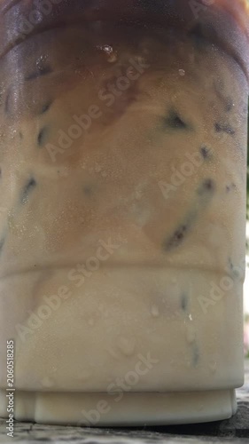 Close up, stirring and mixing an iced latte until the milk has combined with the coffee. 