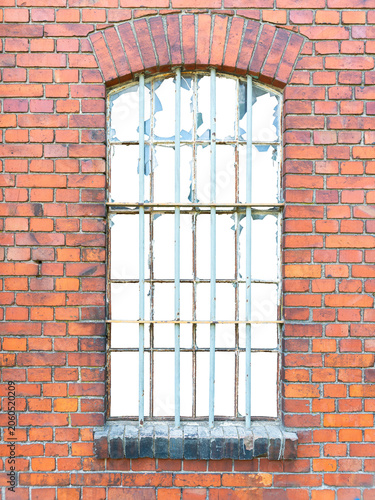 An old window with metal bars in a red brick building with broken windows. The building's interior is isolated.