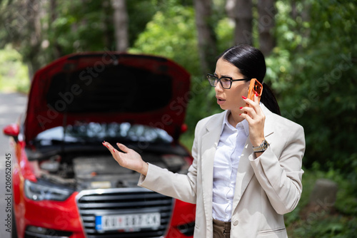 Fotografía Frustrated businesswoman standing beside her broken red car with the hood open,