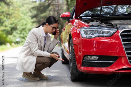 Photography Woman having a car breakdown on the road, talking on smartphone for assistance w