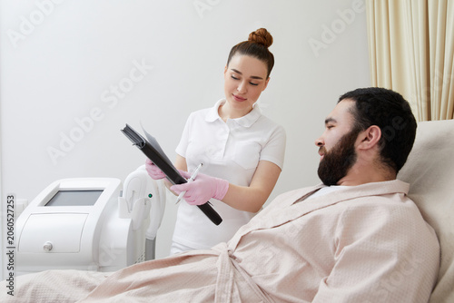 Bilde på lerret Professional cosmetician woman with papers talking to man before procedure in cl