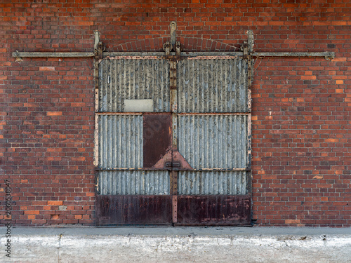 An old rusty gate with a metal sliding door in a red brick building.