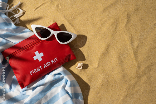 First aid kit and sunglasses on beach towel for travel safety and summer health essentials