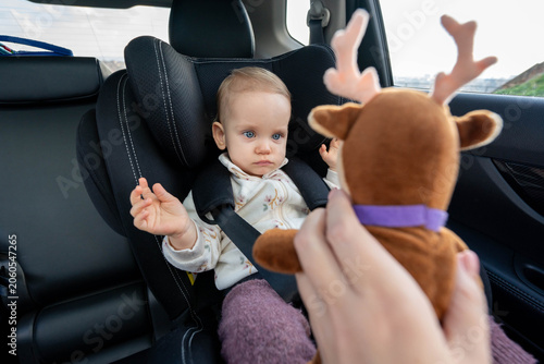 Fotografija Mother trying to entertain baby in car seat with a toy