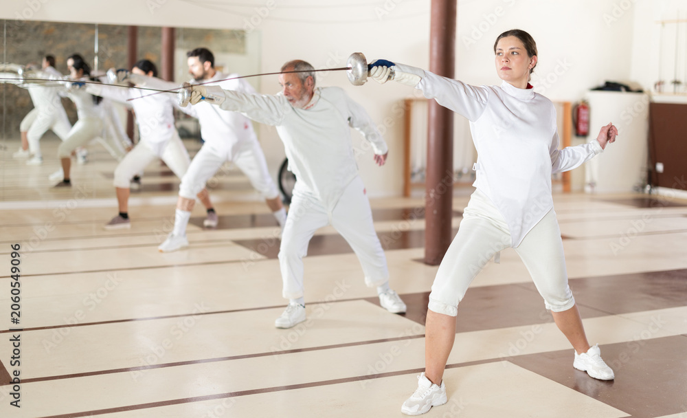 Fototapeta premium Men and women in white uniforms practice fencing techniques with foils in their hands