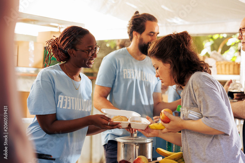 Schilderij op canvas African american volunteer lady at local center actively involved in distributing nutritious meals to alleviate hunger among the less fortunate; black woman helper sharing food to homeless person