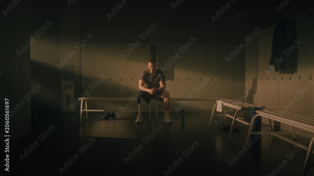 Fototapeta premium Athlete with Bionic Leg Sitting in Beam of Light. Man Transitions From Pensive Look Toward Window to Sharp, Inspired, and Strong Expression. Intersection of Vulnerability and Empowerment. Portrait.