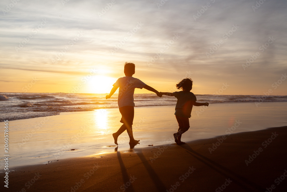 Fototapeta premium Happy Children Silhouette Running and Holding Hands on the Beach at Sunset