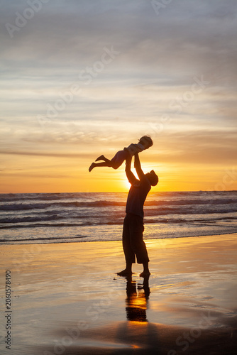 Father lifting young child in the air on beach at sunset, silhouette