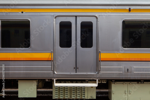 Side View of a Stainless Steel Passenger Train Car with Closed Sliding Doors, Windows, and Yellow Stripe Accents