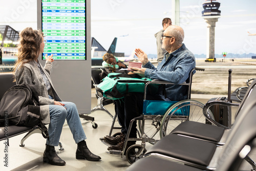 Foto Woman traveling with old man wheelchair user, mobility aid in airport terminal, happy pensioners traveling together, senior couple breaking stereotypes, representing inclusion and freedom