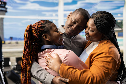 Foto Emotional moment of black parents embracing young girl in airport terminal, saying a bittersweet goodbye before boarding international flight