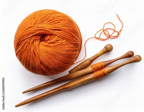 top view of a ball of orange wool yarn with a loose thread and two vintage wooden spindles for spinning isolated on a white background representing traditional handicraft and textile arts