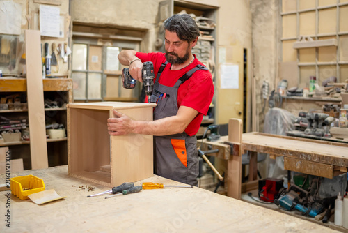 Принти на полотні Carpenter assembling wooden cabinet using cordless drill in workshop