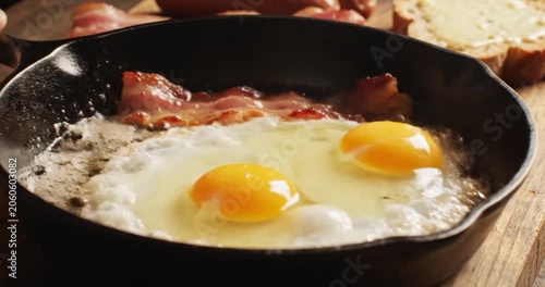 Two Fresh Eggs Frying with Bacon in a Cast Iron Skillet for Breakfast