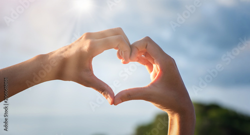 Girl hands in shape of love heart on blue sky with cloud.