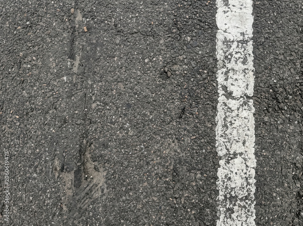 Fototapeta premium Close-up of weathered asphalt road surface with a white line marking