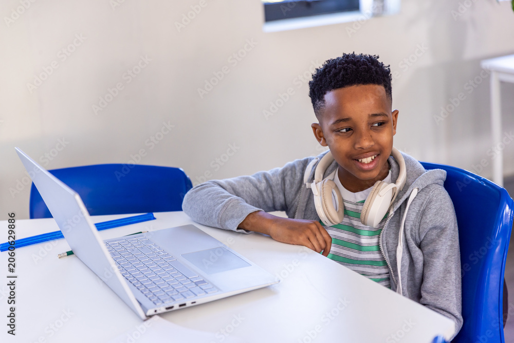 Naklejka premium African American boy child sitting in class with gray hoodie, white headphones, silver laptop