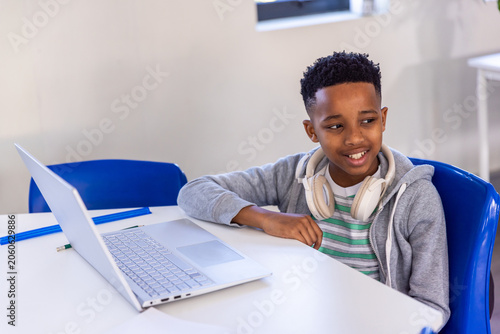 African American boy child sitting in class with gray hoodie, white headphones, silver laptop