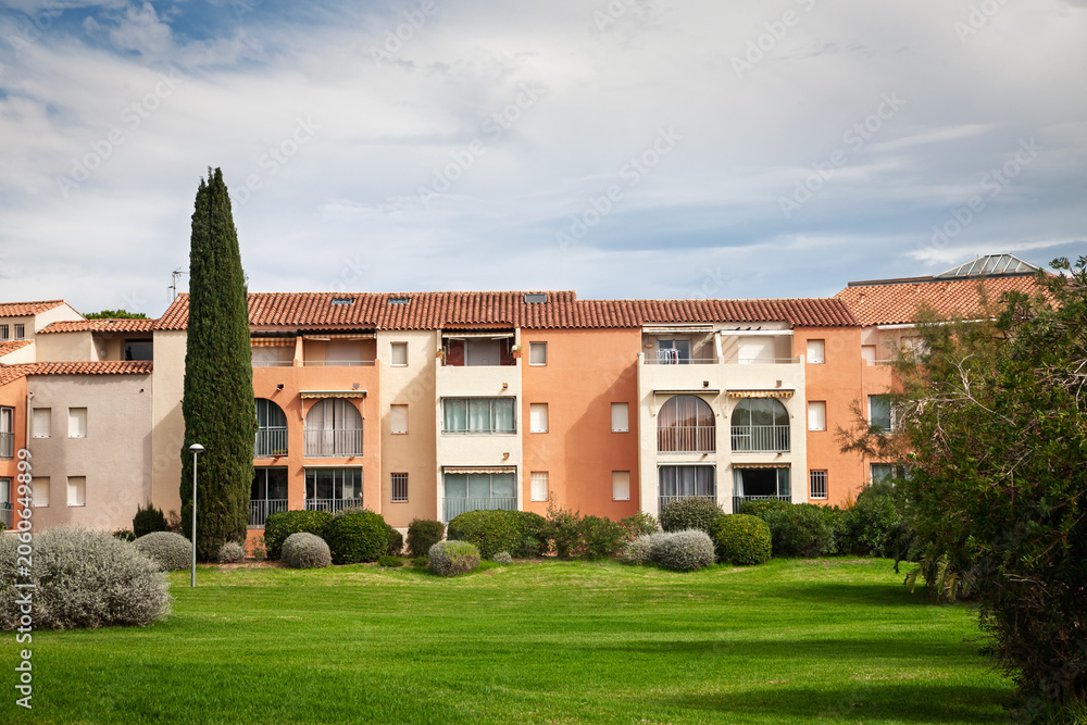 Fototapeta premium Holiday residence on the French Riviera, with pastel apartment buildings, terracotta roofs, balconies, cypress tree, gardens and lawns showing Mediterranean real estate and vacation housing in france.