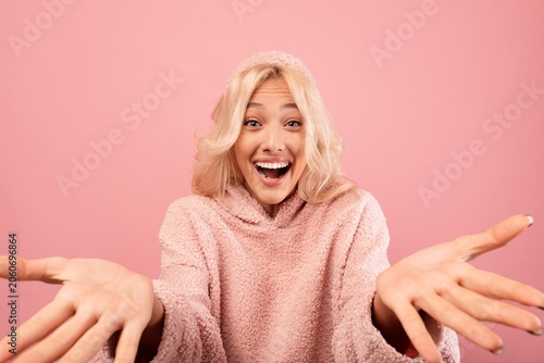 Принти на полотні Smiling Young Woman With Light Complexion Gesturing With Outstretched Hands In Joyful Emotion, Standing Against Pink Background