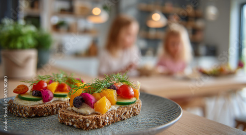 Open faced sandwich with fresh vegetable toppings on whole grain bread served on plate, two children blurred in background playing happily