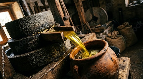 Traditional stone mill pressing fresh golden olive oil into a pot