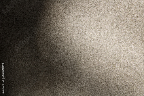 A finely textured stucco wall surface showcasing a dramatic lighting transition. From deep shadow on the left into a warm, bright spotlight on the right.