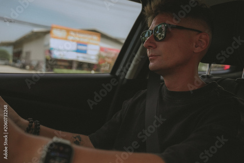 A man driving a car on a busy road, dashboard and steering wheel in focus with sunlight entering through the windshield.