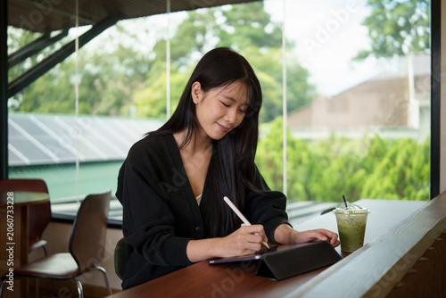 Fotografía Young woman using a digital tablet with stylus pen while sitting in a modern cafe