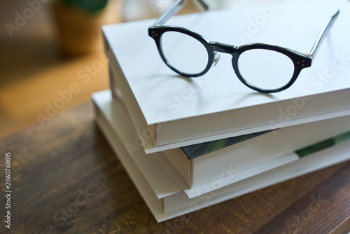 Glasses on stack of books on wooden desk with natural light
