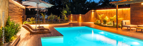 Luxury swimming pool with wooden deck and cozy lighting at night. Concept of relaxing outdoor living space