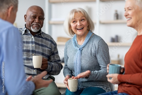 Photos Joyful Elderly Caucasian Woman Sitting With Two Other Adults, Engaging In Conversation Over Coffee In Modern Office Setting