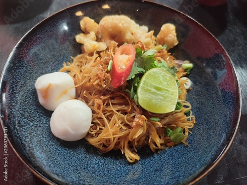 Traditional stir-fried noodles topped with crispy pork rinds, fish balls, and chopped cilantro.
