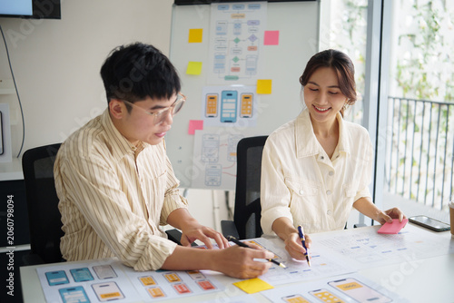 Fotografie Two UX designers collaborating on mobile app wireframes, reviewing paper prototypes and user interface layouts in a bright office