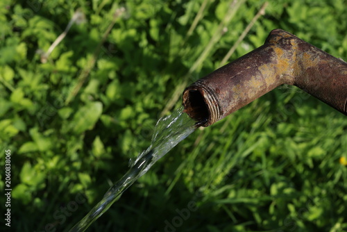 Rusted pipe drips clear water into grassy field