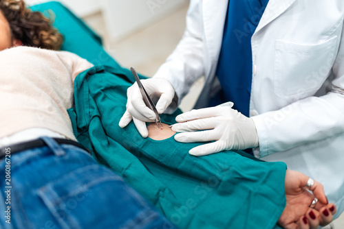 A surgeon uses medical forceps and a scalpel for a mole removal procedure or skin biopsy on a patient. Clinical dermatology service, minor outpatient surgery,
