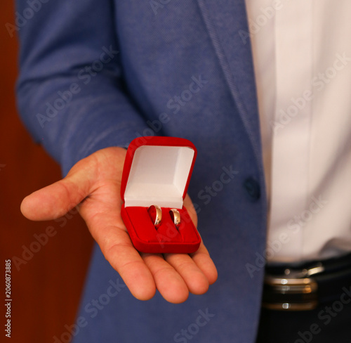 Hand holds open red ring box with two gold rings