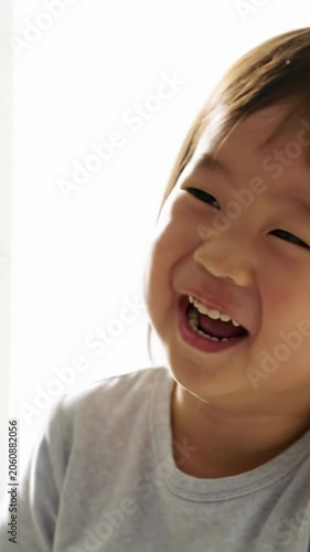 A radiant young child with a natural appearance, smiling and laughing joyfully. Medium close-up video, creamy bokeh background, high-key natural light. Concept of pure childhood joy