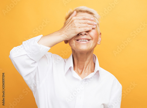 Elegant senior blonde woman making a bold facepalm gesture on a yellow background