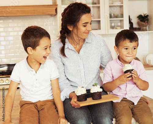 Mom and two little boys, brothers, are eating homemade cupcakes.