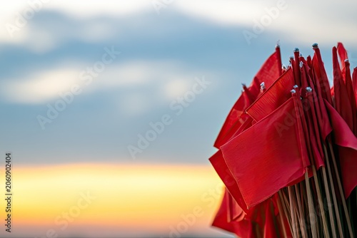 Many small red flags clustered together, silhouetted against a soft sunset sky