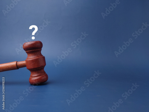 A brown wooden judicial gavel stands upright against a blue background surface below a white question mark icon