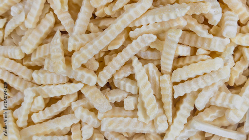 A close-up, top-down view of a large pile of uncooked, frozen crinkle-cut potato fries, ready for cooking. The texture and irregular shapes create an appealing pattern for food preparation concepts