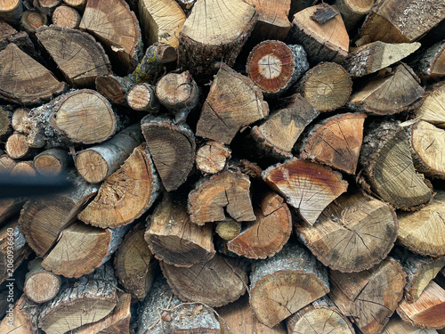 Full frame texture photo of a large, dense stack of seasoned firewood, featuring varied split logs and rough bark patterns under diffuse daylight