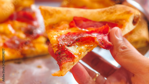 Schilderij op canvas Hand holding a fresh hot slice of pepperoni pizza with melted cheese and crispy