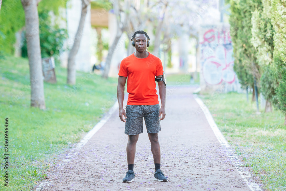 Obraz premium Athlete standing on a park path, listening to music and wearing a smartphone armband